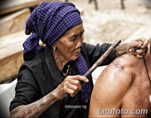 Фото процесса нанесения традиционной татуировки вручную пожилой женщиной. Виден инструмент для татуировки и кожа клиента.