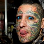 Фотография мужчины с экстремальными татуировками на лице и теле, с яркими голубыми глазами и необычным внешним видом.