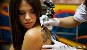 Фотография процесса нанесения татуировки на спину девушки, мастер в перчатках работает тату-машинкой, девушка выглядит немного напряженной.