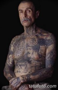 Фотография пожилого мужчины с множеством татуировок на теле, демонстрирующих его богатый жизненный опыт.
