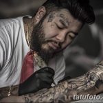 Фотография мастера тату, делающего татуировку на руке клиента. Мастер сосредоточенно смотрит на свою работу.