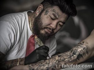 Фотография мастера тату, делающего татуировку на руке клиента. Мастер сосредоточенно смотрит на свою работу.