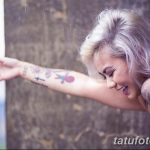 Фото тату: девушка с татуировками на руках, стоящая под дождем. Видны татуировки в виде цветов, геометрических узоров и надписей.
