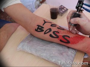 Фото процесса татуировки: мастер наносит надпись 'Yes Boss' на руку клиента.