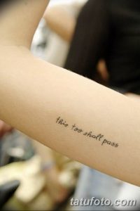 Фото тату надписи на руке. Текст 'this too shall pass' выполнен простым шрифтом черными чернилами. Минималистичный дизайн.