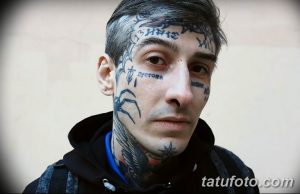 Фото мужчины с множеством татуировок на лице, шее и теле. Татуировки включают надписи, символы и рисунки.