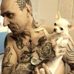Фото мужчины с множеством татуировок на теле, держащего на руках маленькую собачку чихуахуа.