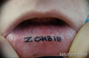 Фото татуировки на внутренней стороне губы: надпись "ZOMBIE" черным цветом, выполненная небольшим шрифтом.