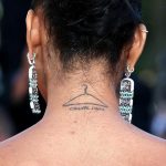 Фото тату вешалки для одежды с надписью "CHANEL Iman" на затылке. Рисунок выполнен в минималистичном стиле черными чернилами.