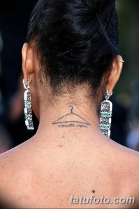 Фото тату вешалки для одежды с надписью "CHANEL Iman" на затылке. Рисунок выполнен в минималистичном стиле черными чернилами.
