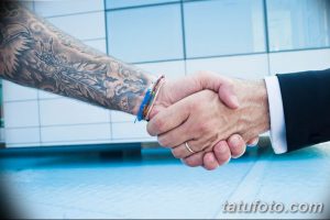 Фото рукопожатия, на котором видно татуированное предплечье с изображением дракона. Черно-серые тона.