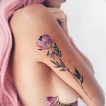 Фотография цветной татуировки на боку женщины, изображающей ветку с цветущими пионами. Использованы нежные пастельные тона.