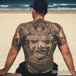 Фотография масштабной татуировки на спине мужчины, изображающей японского самурая в маске. Детализированный рисунок выполнен в реалистичном стиле с использованием черных и серых оттенков.