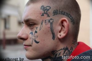 Фото мужчины с татуировками на лице, шее и голове. Изображения животных, надписи и символы покрывают большую часть его лица.