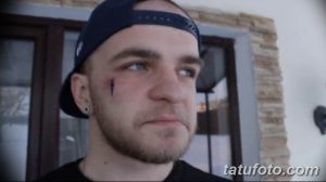 Фото минималистичной татуировки в виде черной слезы под глазом мужчины. Простой и лаконичный рисунок.