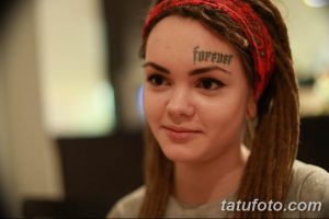 Фото тату: девушка с татуировкой надписи "Forever" на лбу. Рисунок выполнен черными чернилами.
