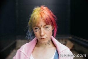 Фото тату девушки с надписями 'TEAR' и 'HOPE' под глазами. Волосы девушки окрашены в радужные цвета.