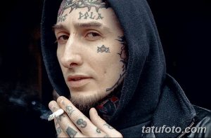 Фото тату: татуировка на лице мужчины, изображающая мрачный и загадочный образ с надписями и символами. Экстремальный и выразительный дизайн.