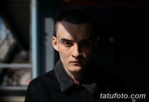Фото тату на лице молодого человека: небольшая татуировка в виде геометрической фигуры рядом с глазом. Минималистичный стиль.