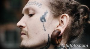 Фото тату на лице мужчины: небольшой рисунок одуванчика с семенами, выполненный в технике лайнарт.