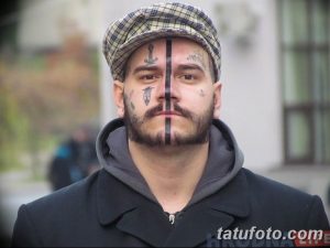 Фото тату: лицо мужчины, покрытое сложными татуировками, имитирующими усы и другие символы. Экстремальный рисунок татуировки.
