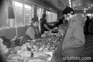 Фото мужчины с татуировками на лице и шее. Изображены различные рисунки и надписи, выполненные в черно-белом стиле. Фотография сделана в черно-белом формате.