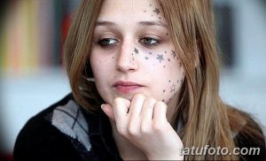 Фото татуировок в виде маленьких звездочек на лице девушки. Татуировки расположены вокруг глаз и на щеках. Стиль татуировки - минимализм.