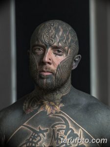 Фотография мужчины с полностью татуированным лицом, шеей и головой. Татуировки выполнены в черном и сером цветах и имеют сложный узор.