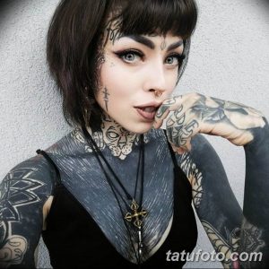 Фотография девушки с обилием татуировок на лице, шее, руках и теле. Татуировки выполнены в черном цвете и имеют сложные узоры.