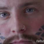 Фотография мужчины с геометрическими татуировками, покрывающими его щеки и часть лба. Татуировки выполнены в сером цвете и имеют сложный узор.