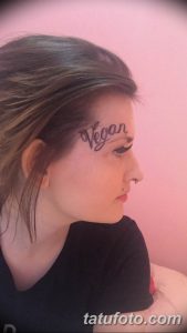 Фото тату: Девушка с татуировкой надписи "Vegan" на лице, рядом с бровью. Минималистичный стиль и акцент на идеологии.