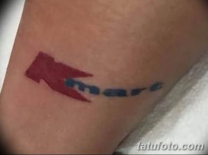 Фото тату с изображением красной стрелки и надписи 'kmart' на руке. Простой, минималистичный рисунок.