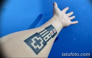 Фото тату с изображением контроллера D-Pad от Nintendo, выполненного в минималистичном черном стиле на предплечье.
