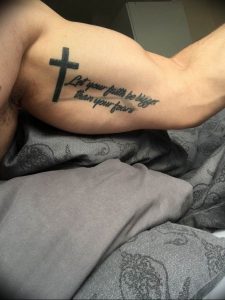 Фото тату на предплечье с изображением креста и надписью 'Let your faith be bigger than your fears'. Черно-белый рисунок в каллиграфическом стиле.