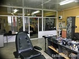 Фото тату-студии с большими окнами, черным креслом и множеством инструментов для татуировки. Светлое и просторное помещение.
