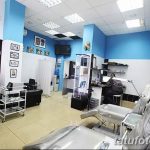 Фото тату-студии с голубыми стенами, двумя кушетками и множеством инструментов для татуировки. Современный дизайн и яркое освещение.