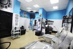 Фото тату-студии с голубыми стенами, двумя кушетками и множеством инструментов для татуировки. Современный дизайн и яркое освещение.