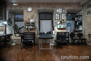 Фото тату-студии с кирпичной стеной, черной мебелью и несколькими кушетками для клиентов.