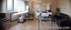Фото тату-студии в светлых тонах с белой кушеткой, современным оборудованием и большим окном.