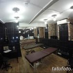 Фото тату-студии с черными стенами, двумя кушетками и гитарой на стене. Современный дизайн и профессиональное оборудование.