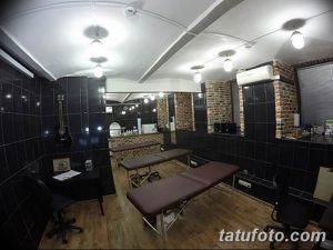 Фото тату-студии с черными стенами, двумя кушетками и гитарой на стене. Современный дизайн и профессиональное оборудование.