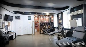 Фото просторной тату-студии с несколькими рабочими местами, удобными креслами и телевизором. Современный и функциональный интерьер.
