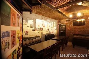 Фото интерьера тату-студии с кирпичными стенами, деревянной мебелью и постерами с рисунками татуировок. Атмосфера свободы и творчества.