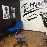 Фото интерьера тату-студии с постерами, тату-машинами и удобным креслом для клиента. Стены украшены рисунками и надписями.