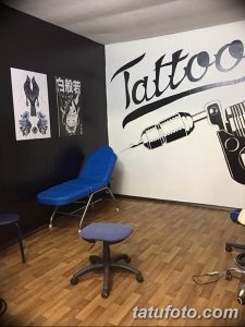 Фото интерьера тату-студии с постерами, тату-машинами и удобным креслом для клиента. Стены украшены рисунками и надписями.
