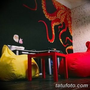 Фото интерьера тату-студии с большим изображением красного осьминога на черной стене, яркой мебелью и оригинальным декором.