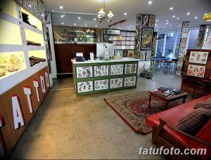 Фото ресепшн и зоны ожидания в тату-салоне с яркой вывеской 'TATTOO', удобной мебелью и множеством эскизов на стенах.
