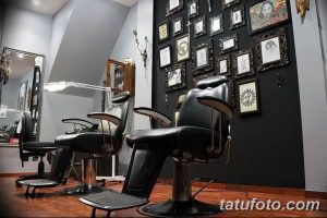 Фото современного интерьера тату-салона с черными креслами для клиентов и стеной, украшенной черно-белыми эскизами татуировок.