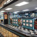 Фото тату салона с черно-белой плиткой на полу. Видны стойка ресепшн, кресла для ожидания и стены, украшенные эскизами татуировок.
