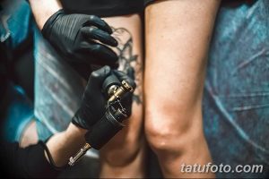 Фото тату процесса нанесения рисунка на ногу. Мастер в черных перчатках работает машинкой. Крупный план.